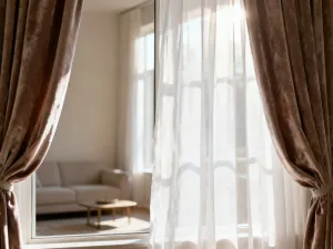 Beżowa roleta plisowana zamontowana bezinwazyjnie na ramie dużego, nieotwieranego okna w nowoczesnym salonie.